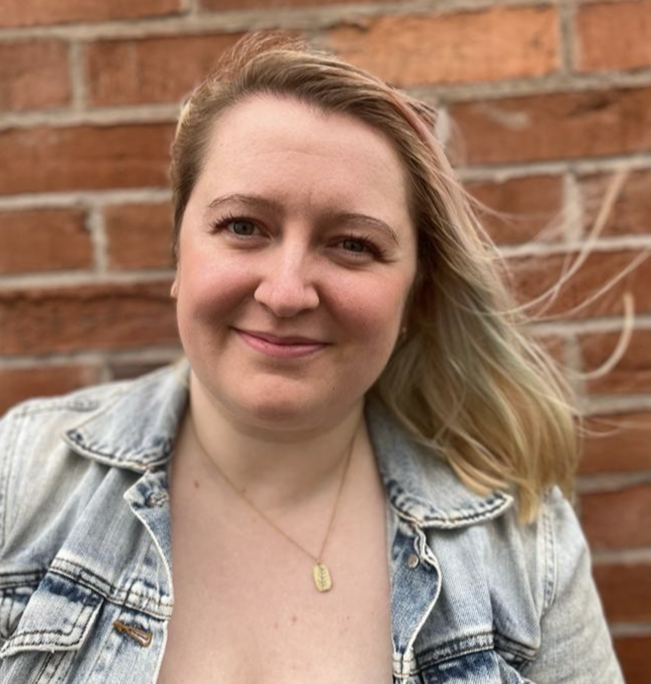 Profile of light-skinned woman with blond hair wearing a jean jacket smiling at you.