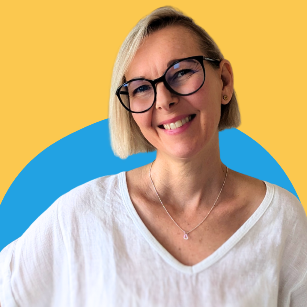 Lia Stoll is standing in front of a blue and yellow wall, wearing dark-framed glasses and a white shirt is smiling at you.